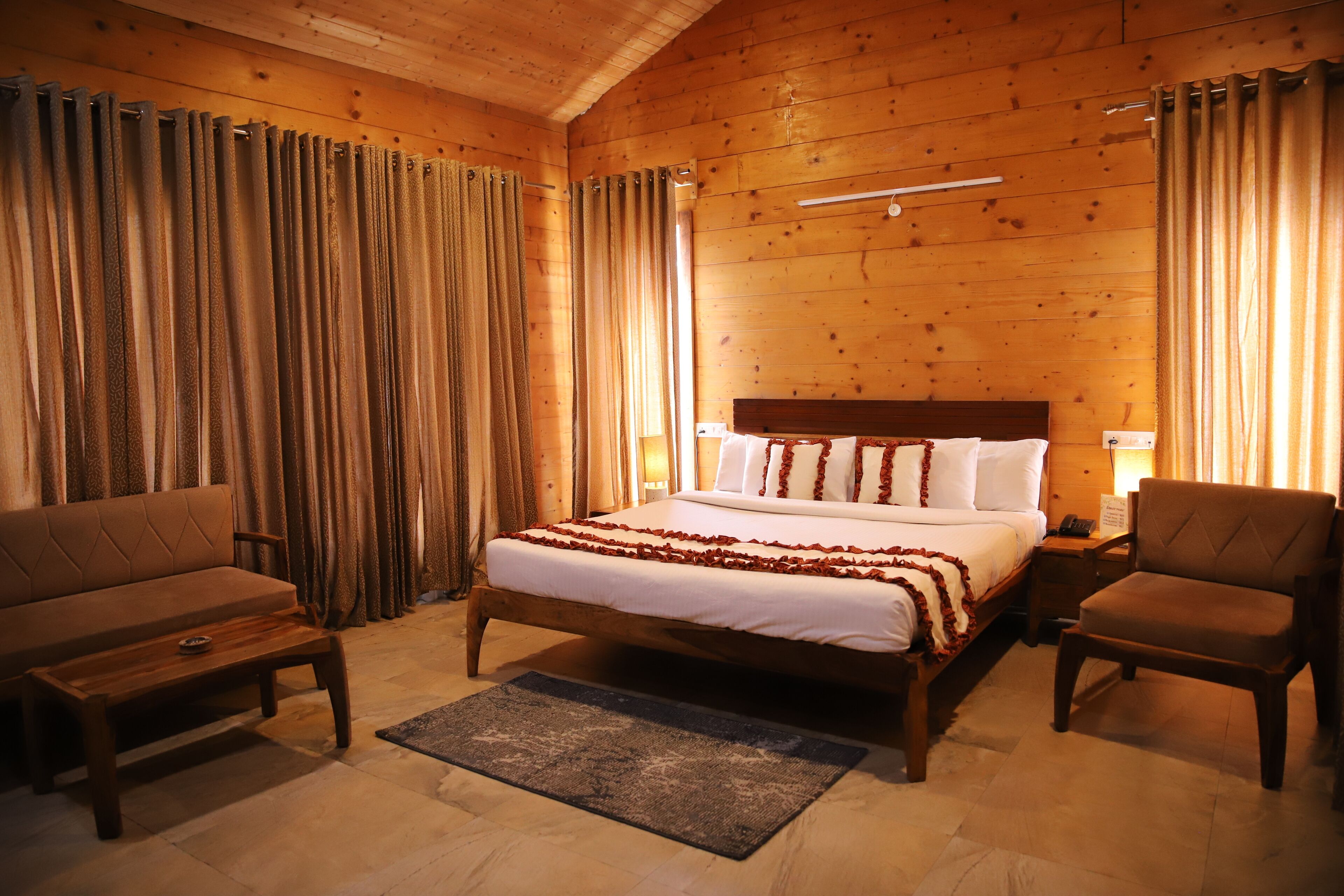 Una habitación con paneles de madera, una cama, un sofá, una silla y una mesita de noche.