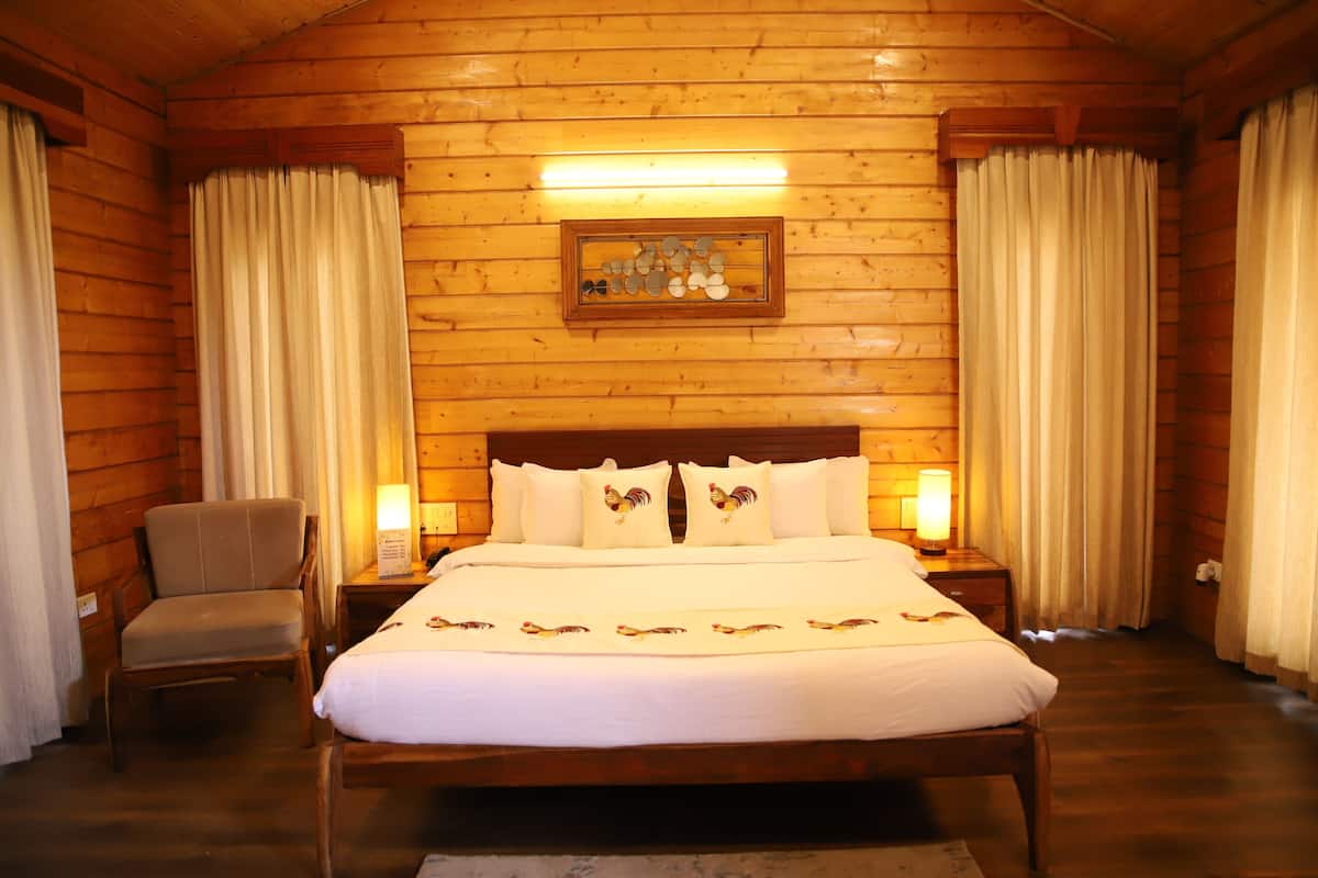 A wooden cabin-style room with a large bed, two bedside tables, a chair, and curtains.