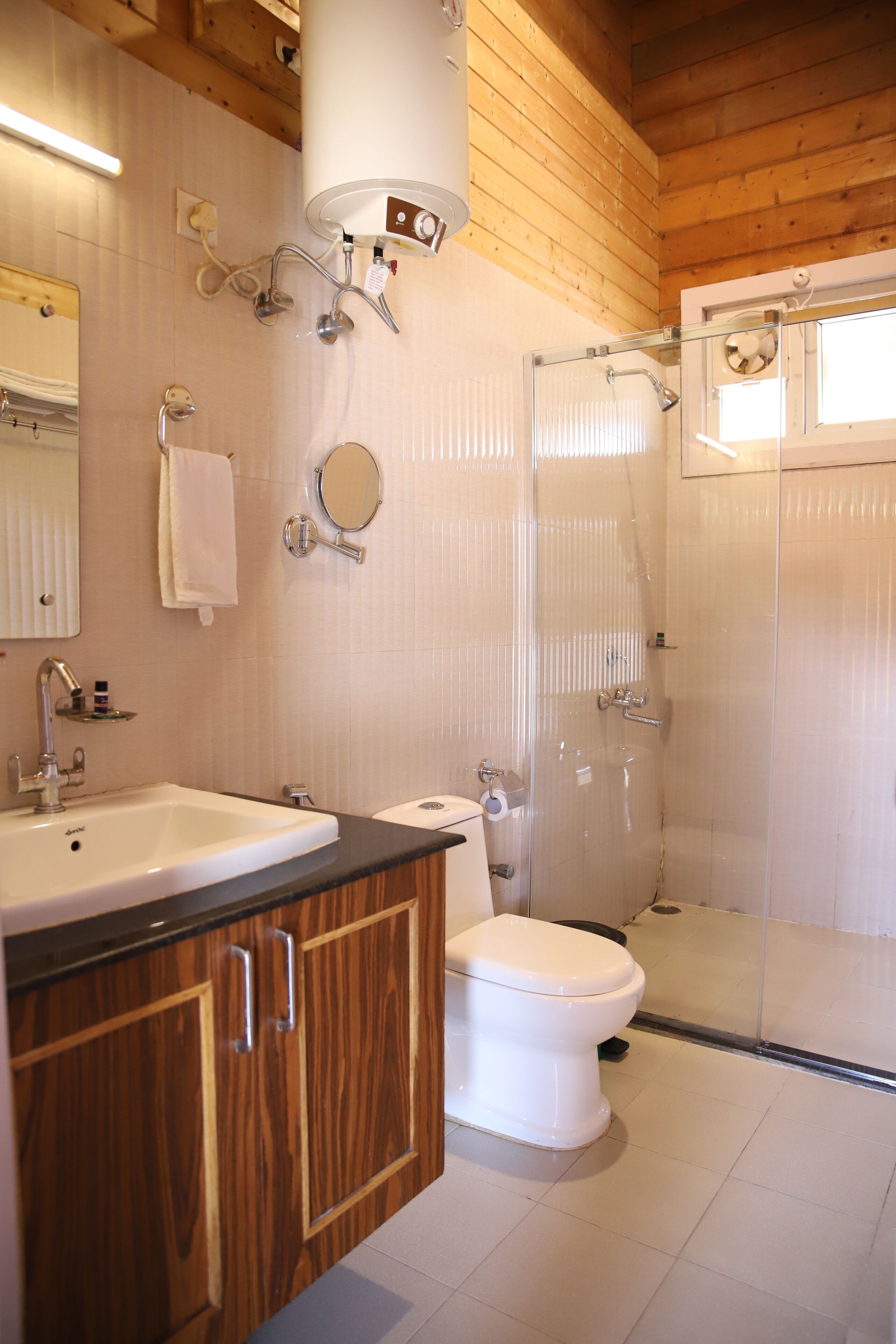 A bathroom with a wooden ceiling, a white sink, a toilet, and a glass-enclosed shower.