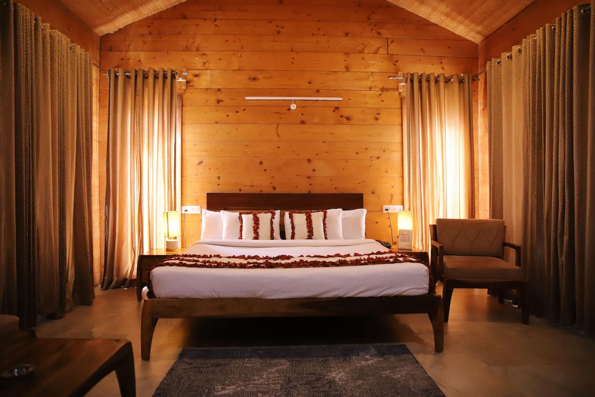 A wooden-paneled bedroom with a large bed, a chair, and curtains.