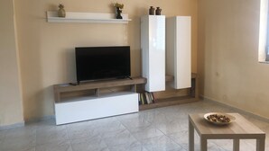 A modern living room with a flat-screen TV on a wooden stand, a white cabinet, and a small table with a bowl of food. - CasaLotto Holiday Home Reggio Calabria (Reggio Calabria)
