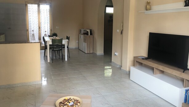 A modern living room with a flat-screen TV, a dining area with a table and chairs, and a kitchen area with a microwave. - CasaLotto Holiday Home Reggio Calabria (Reggio Calabria)