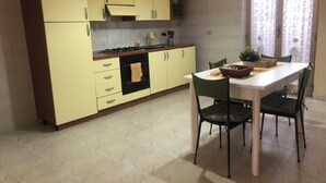 A kitchen with yellow cabinets, a white dining table, and a window with patterned curtains. - CasaLotto Holiday Home Reggio Calabria (Reggio Calabria)