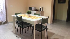 A dining area with a white table, green chairs, a potted plant, and a microwave on a cabinet. - CasaLotto Holiday Home Reggio Calabria (Reggio Calabria)