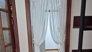 Un couloir doté d’un plancher en bois, d’une porte avec des panneaux en verre dépoli et de rideaux blancs.