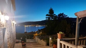 A stone staircase leading to a terrace with potted plants, overlooking a coastal town at night.