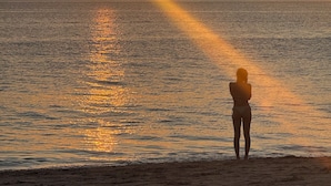A person standing on a beach facing the sunset over a body of water.