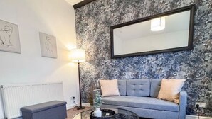 Una sala de estar moderna con un sofá gris, una mesa de centro redonda de vidrio y una pared con textura.