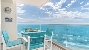 A balcony with a table and chairs, overlooking the ocean.