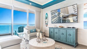 A room with a view of the ocean, a teal cabinet, and a round coffee table with decorative items.
