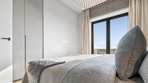 Une chambre moderne avec un grand lit, une armoire et une vue sur l’extérieur grâce à une porte coulissante.