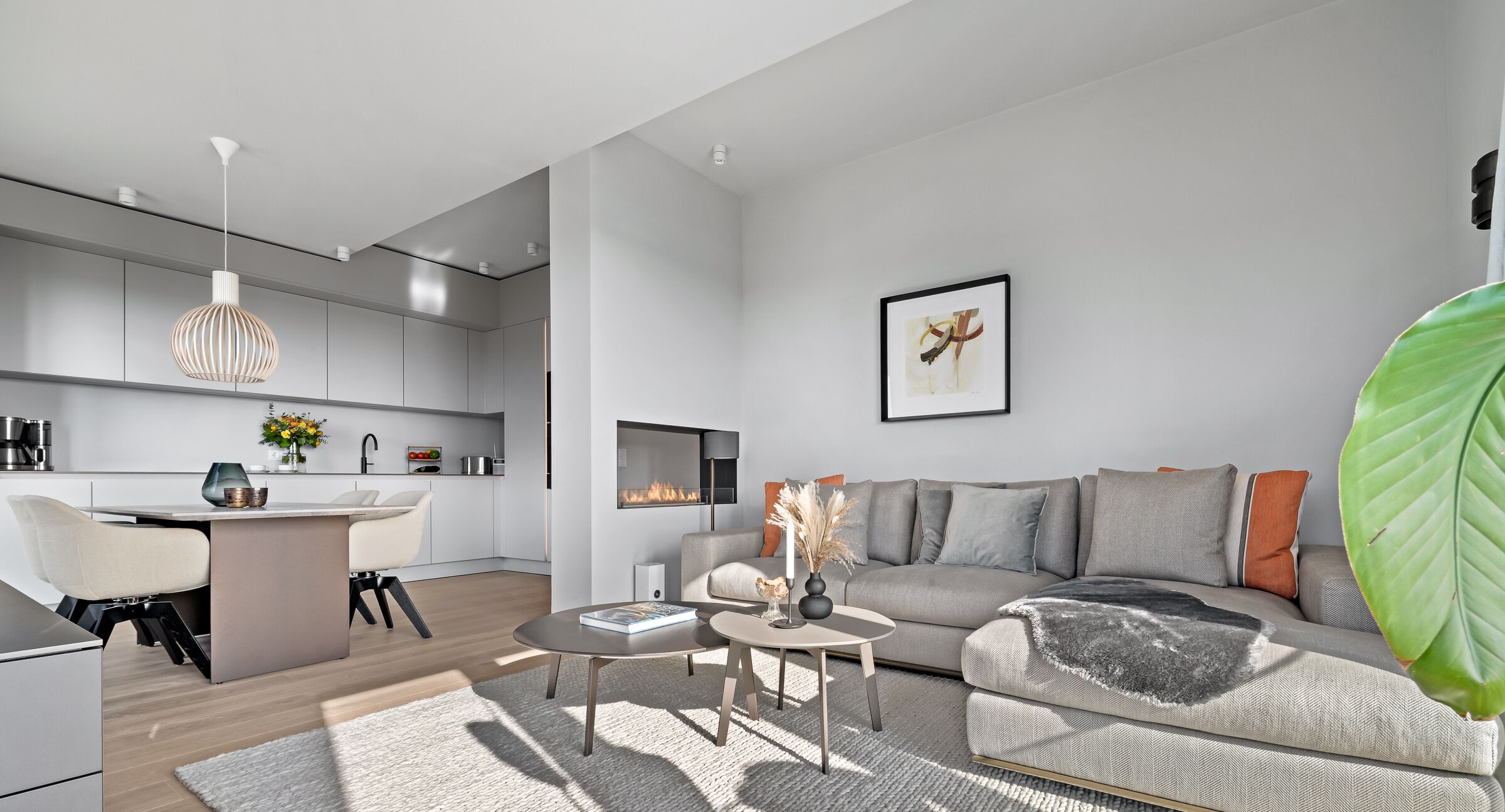 Ein modernes Wohnzimmer mit Sofa, Couchtisch und Kamin. Es gibt eine Küchenzeile mit Schränken und einem Esstisch.