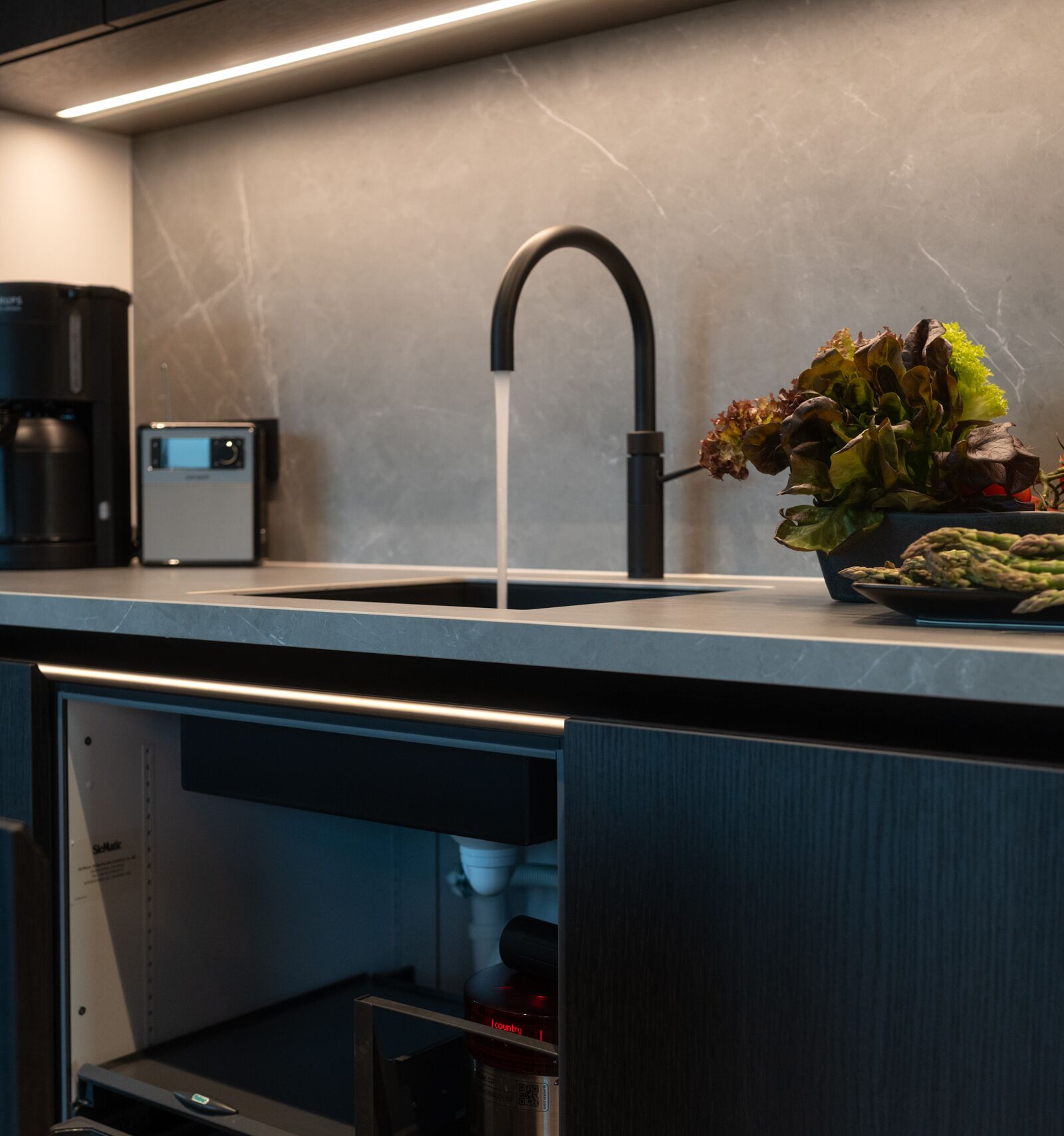Een moderne keuken met een zwarte kraan, een koffieapparaat en een kom groenten op het aanrecht.