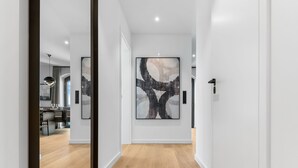 Un corridoio con un grande quadro astratto appeso al muro, un pavimento in legno e una cucina moderna visibile attraverso una porta aperta.