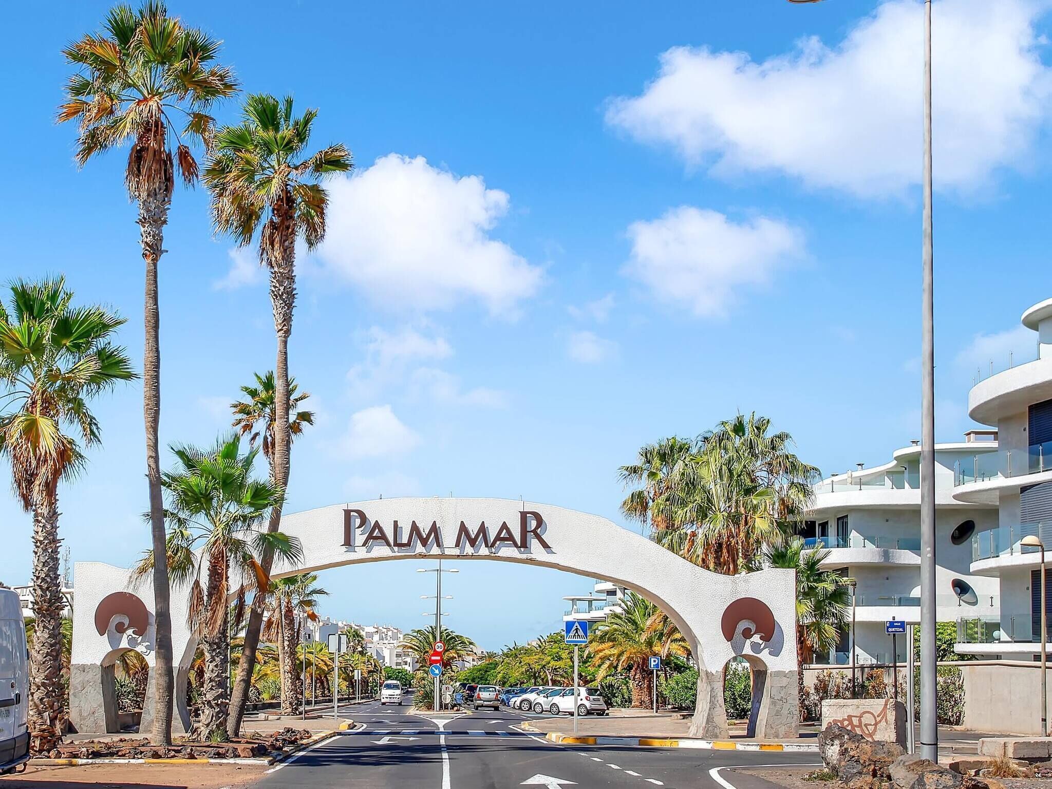 A palm tree-lined street with a sign reading "Palm Mar" above a road.
