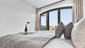 Une chambre moderne avec une grande fenĂŞtre, un lit avec une literie grise, une bouteille de vin et deux verres.
