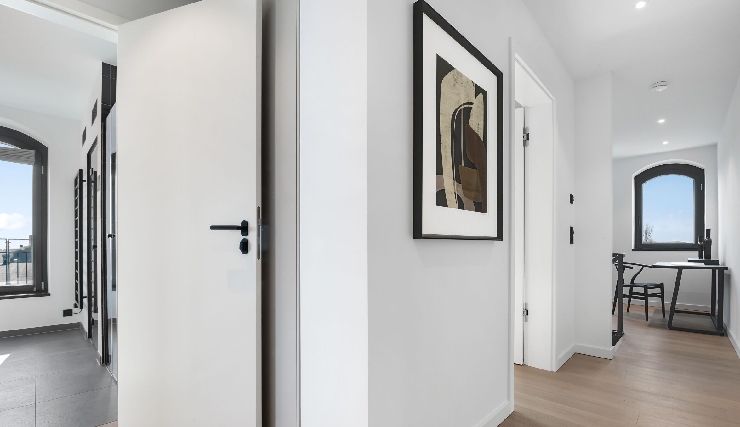 Ein modernes Interieur mit einem Flur, der zu einem Essbereich führt, inklusive eines gerahmten Kunstwerks an der Wand und Blick durch ein Rundbogenfenster.