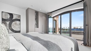 Un dormitorio moderno con una cama grande, un armario y un ventanal que da a un balcón con vistas al mar.