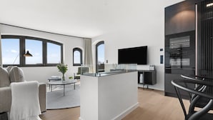Una sala de estar moderna con un sofá, una mesa de centro y un televisor. Cuenta con una zona de cocina con un refrigerador y un microondas.