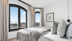 Un dormitorio moderno con un ventanal grande, una cama con ropa de cama gris y un cuadro en la pared.