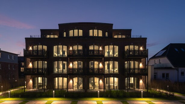 Un edificio de varios pisos con balcones y ventanas amplias, rodeado de un césped cuidado y un sendero.