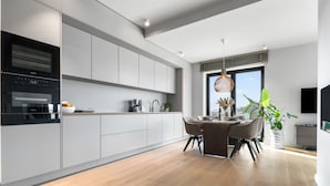 A modern kitchen with grey cabinets, a built-in oven, and a dining area with a table and chairs. - Ocean Breeze Suite - Sea View, Wellness, Ethanol Fireplace, Infrared Cabin (List auf Sylt)