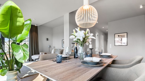 A modern dining area with a wooden table set for two, a hanging light fixture, and a large plant to the left. - Ocean Breeze Suite - Sea View, Wellness, Ethanol Fireplace, Infrared Cabin (List auf Sylt)