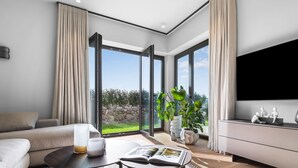 Sala de estar moderna com sofá, mesa de centro, televisão e uma janela grande com vista para o verde.