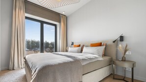 Quarto moderno com uma cama grande, uma mesinha de cabeceira e vista para o verde lá fora.