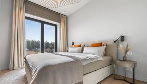 Relax in a spacious room with a large bed, side table, and lamp, offering a view of the outdoors.