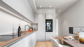 Uma cozinha moderna com bancada comprida, forno embutido e área de jantar com mesa e cadeiras de madeira.