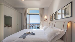 A bedroom with a large bed, a view of the sea through a balcony, and a set of framed pictures on the wall. - ABBRACCIO Amalfi Boutique Retreat (Amalfi)