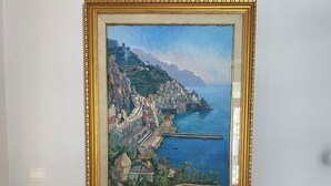 A framed painting of a coastal town, a table with books and a lamp, and a patterned floor. - ABBRACCIO Amalfi Boutique Retreat (Amalfi)