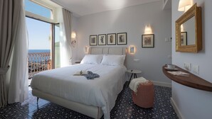 A hotel room with a large bed, a small round ottoman, a bedside table with a lamp, and a view of the sea through a balcony. - ABBRACCIO Amalfi Boutique Retreat (Amalfi)