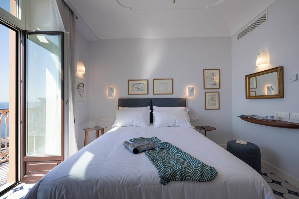A hotel room with a large bed, a balcony, a desk, and a small table.