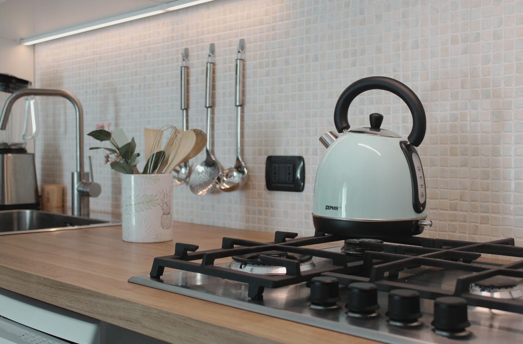 Een keuken met een gasfornuis, een waterkoker en keukengerei dat aan de muur hangt.