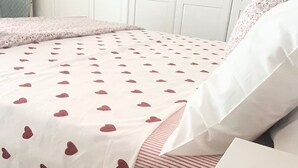 Un lit avec une couvre-lit à motifs blancs et roses, un oreiller rayé et un oreiller blanc.