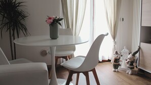 Un coin repas avec une table ronde, des chaises blanches, un vase de fleurs et une plante en pot.