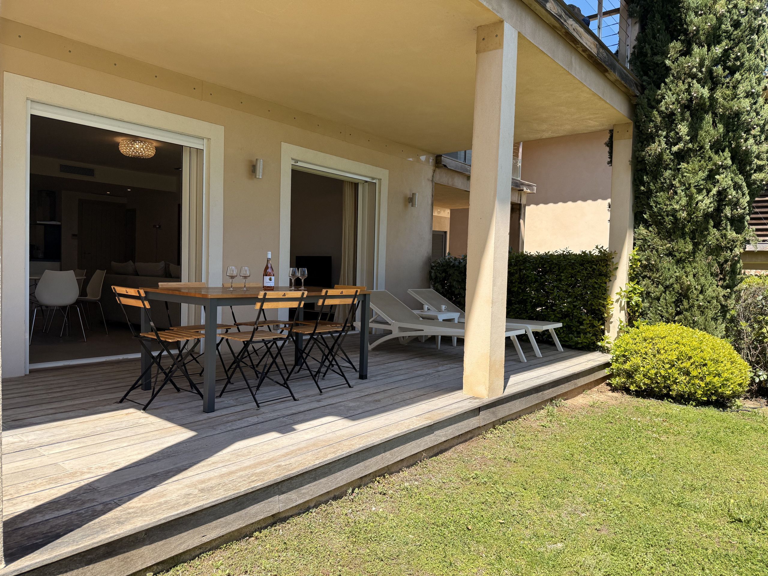 Une terrasse extérieure couverte, avec une table et des chaises en bois, un petit coin salon avec des coussins et une vue sur la verdure environnante.