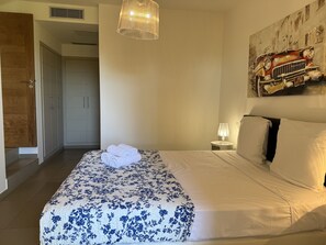 A hotel room with a bed, a painting, a lamp, and a door.