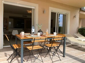 An outdoor dining area with a wooden table and chairs, a vase with flowers, and a view of the interior through an open door. - T4 Côté Plage n°6 by Pinarello Villa Services (Sainte-Lucie de Porto-Vecchio)