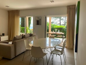 Un salon moderne avec une table à manger ronde, un canapé beige et de grandes fenêtres donnant sur l’extérieur.