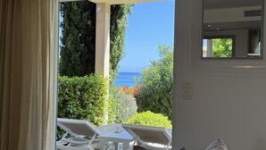 Une pièce avec vue sur la mer, une table blanche avec des chaises et une fenêtre donnant sur un paysage verdoyant.