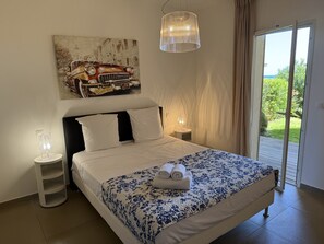 Een slaapkamer met een bed, een schilderij, een lamp en uitzicht door een deur.