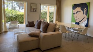 Un salon moderne avec un canapé d’angle, une table à manger avec des chaises, de grandes fenêtres et un tableau accroché au mur.