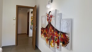 Un couloir orné d’une œuvre d’art moderne au mur, une porte donnant sur une autre pièce et un luminaire placé au-dessus de l’œuvre d’art.