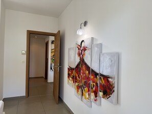 A hallway with a modern art piece on the wall, a door leading to another room, and a light fixture above the art piece.