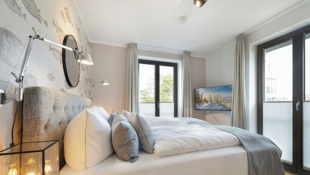 Une chambre à coucher moderne, dotée d’un grand lit, d’un téléviseur fixé au mur et offrant une vue sur l’extérieur grâce à une porte coulissante.