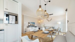 Une cuisine moderne avec des meubles blancs, une table à manger en bois et un coin salon comprenant un canapé et des fauteuils.
