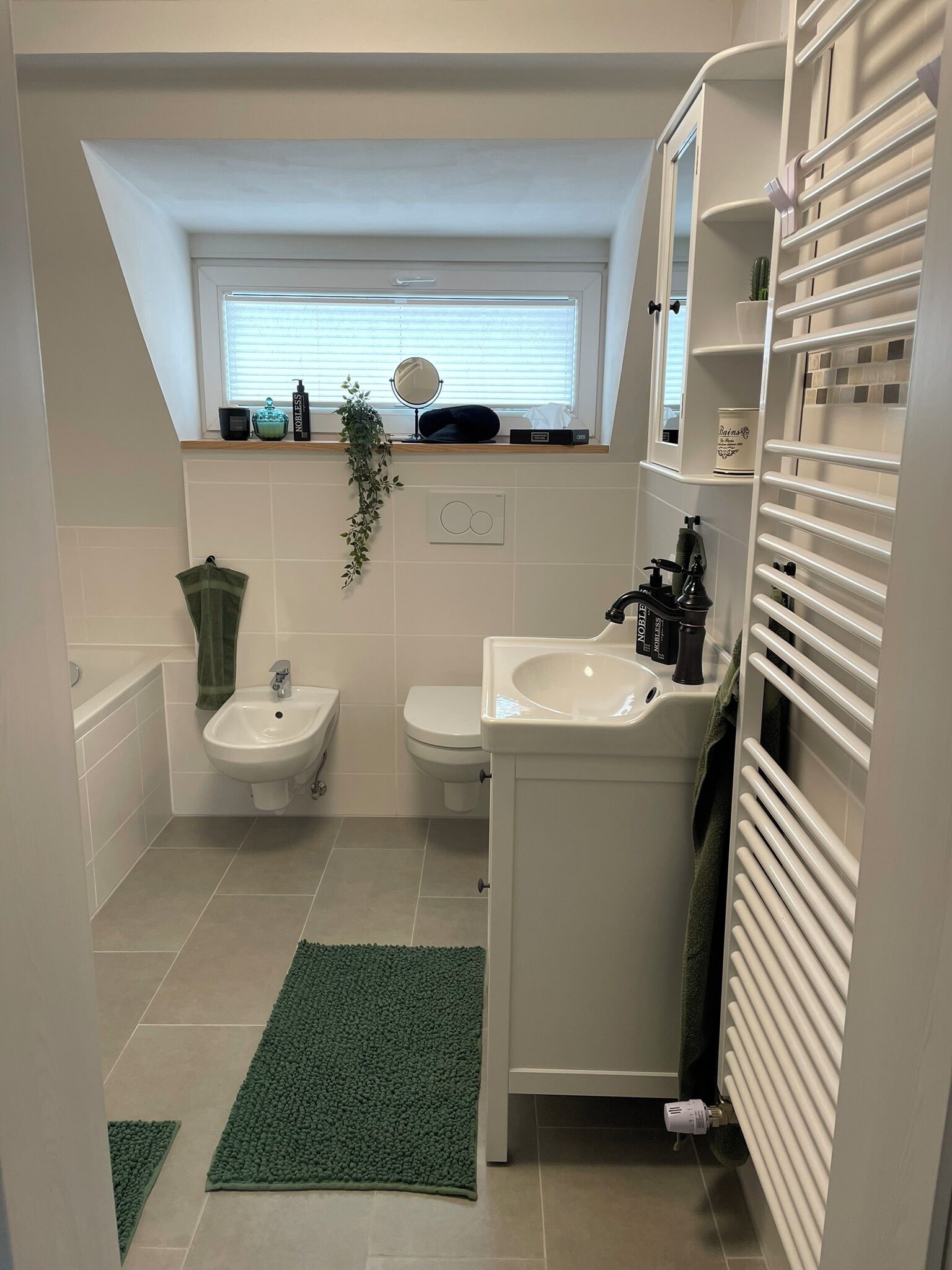 A modern bathroom with a bathtub, a sink, and a toilet. There is a window above the sink and a towel rack beside the toilet.